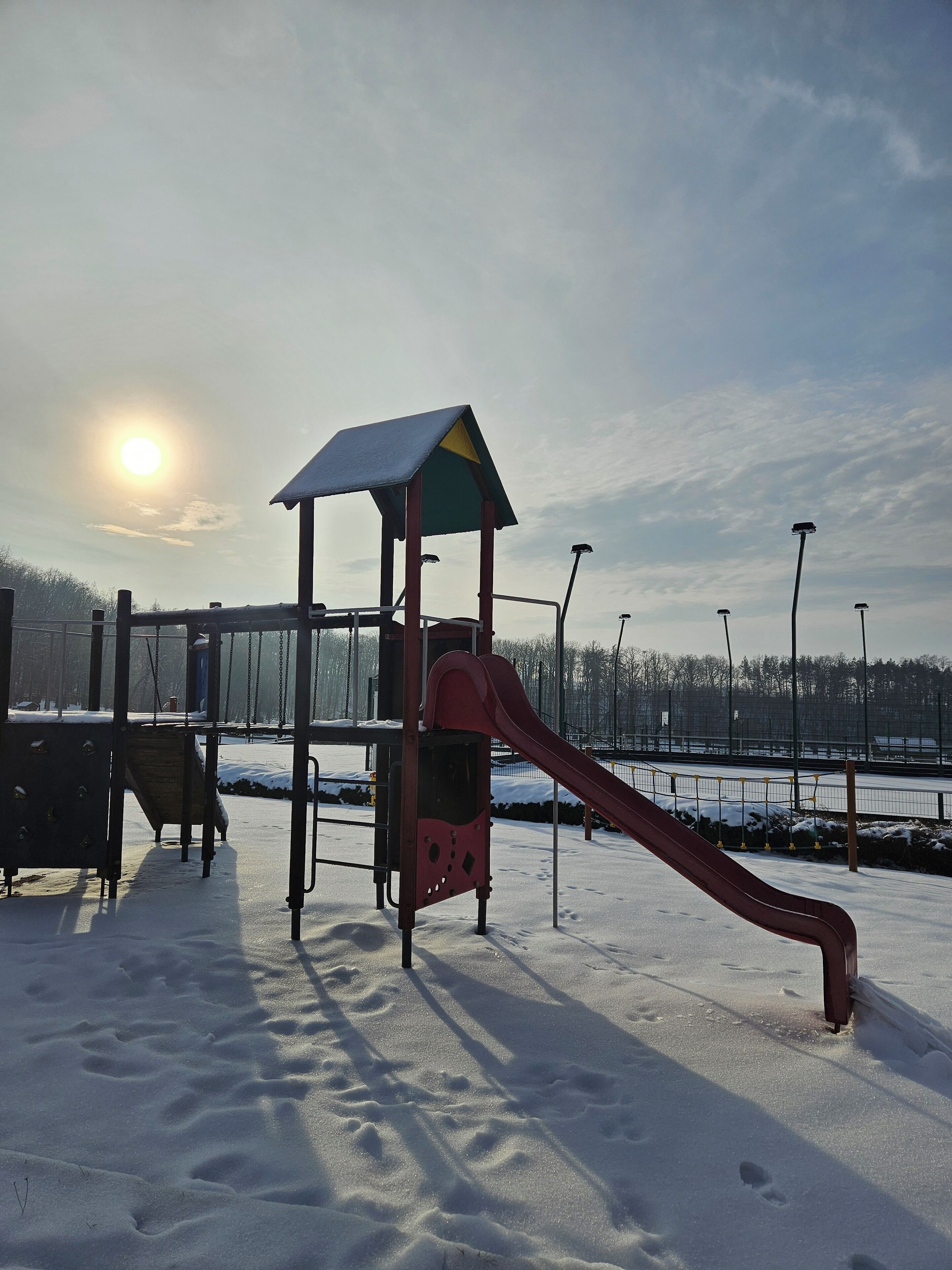 Un parque infantil con tobogán y estructuras para escalar, rodeado de nieve, bajo un cielo despejado.