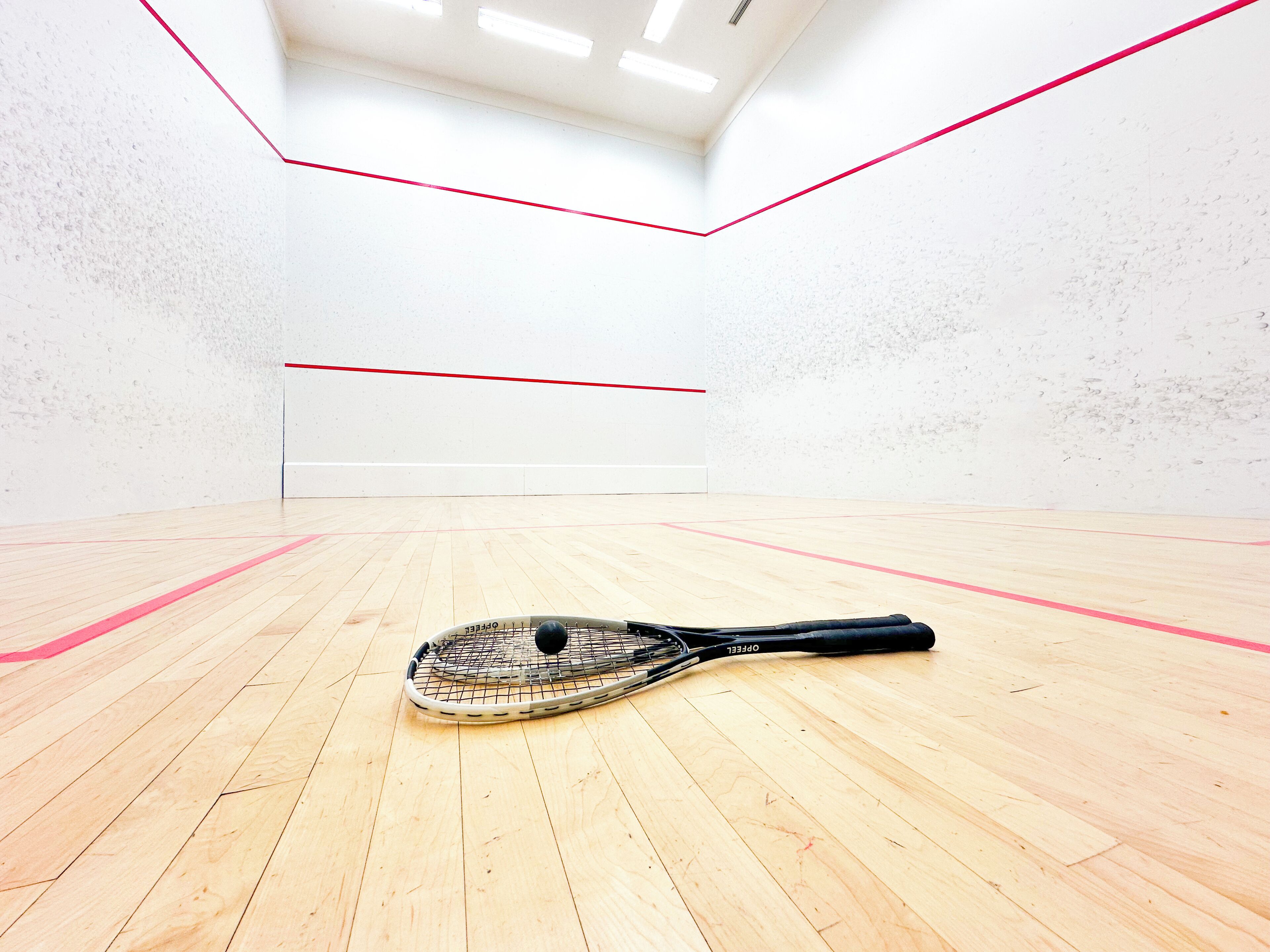 Een squashbaan met een houten vloer en één squashracket.