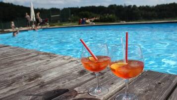 Dos vasos de cóctel rojo con pajitas en una terraza de madera junto a una piscina.