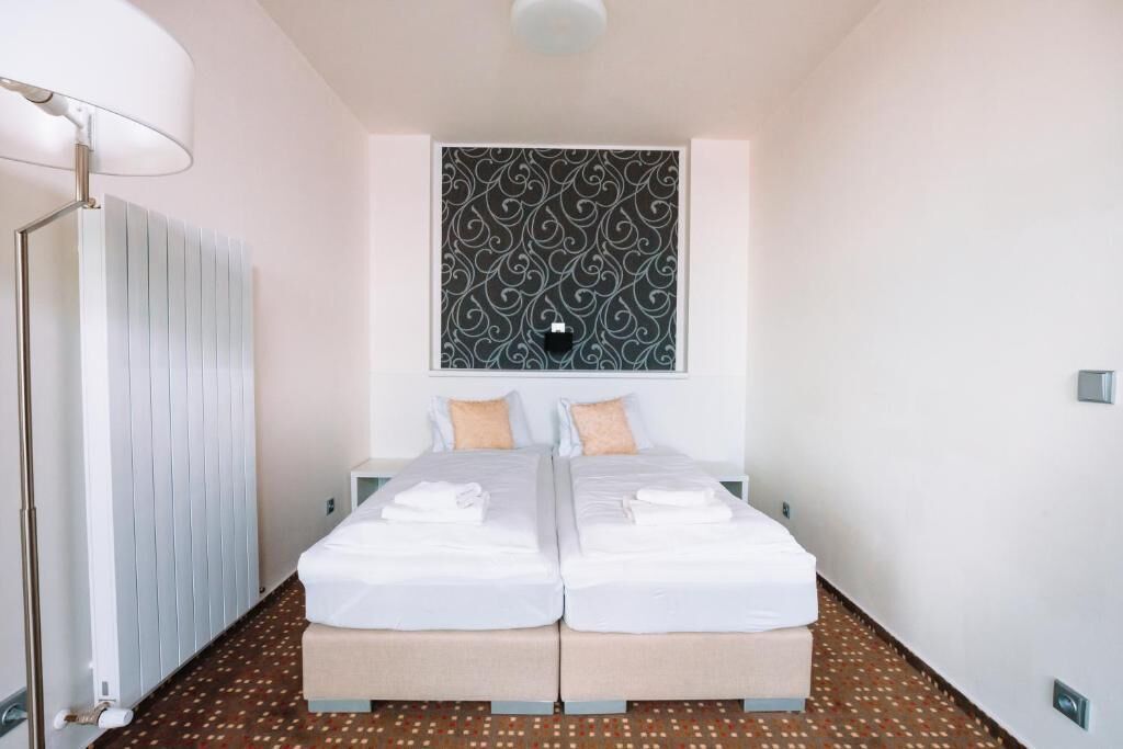 A double room with two beds, a radiator, a patterned wall, and a floor with a geometric pattern.