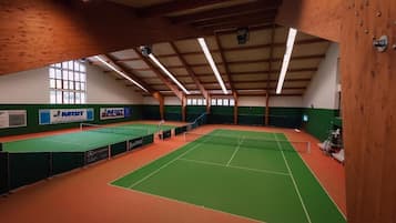 Sisätilojen tenniskenttä, jossa on vihreä ja oranssi lattia, puiset palkit ja korkea katto.