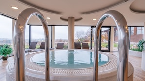 A modern indoor pool with clear glass walls, allowing views of the outside. - K-Triumf resort (Velichovky)