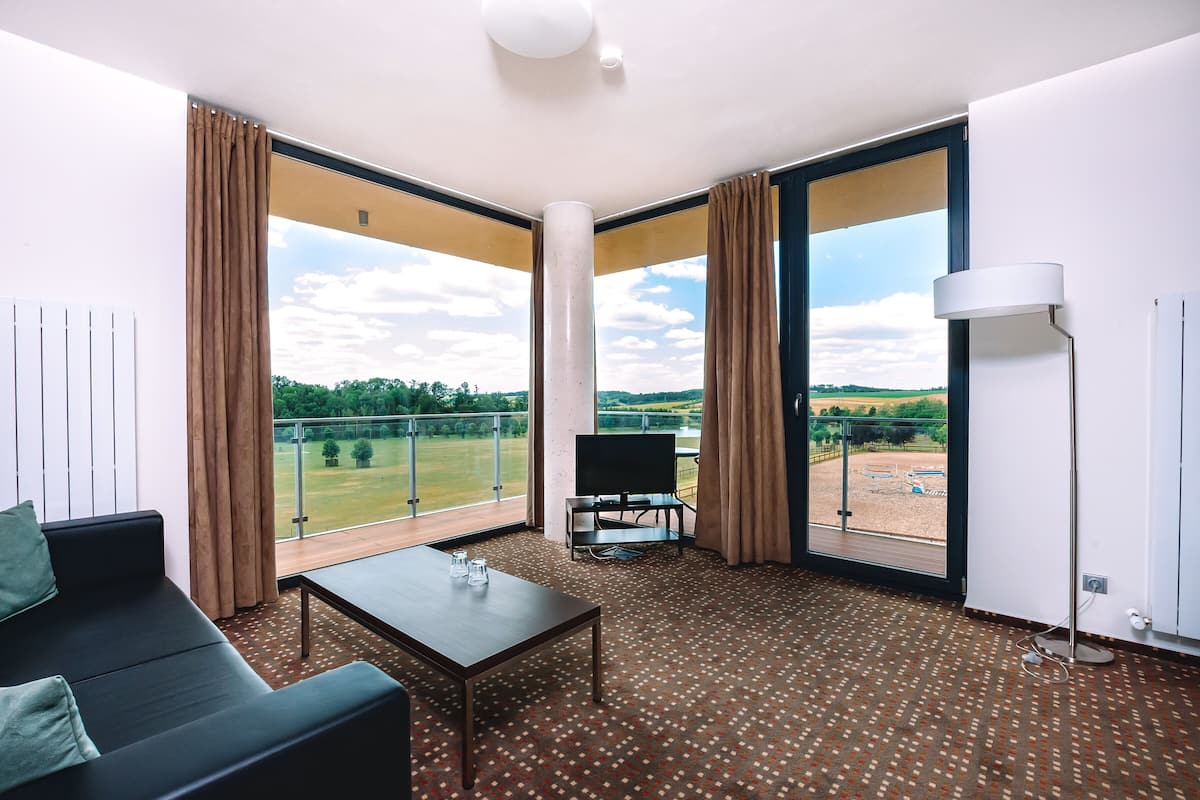 A modern hotel room with a large window, a sofa, a table, and a lamp.