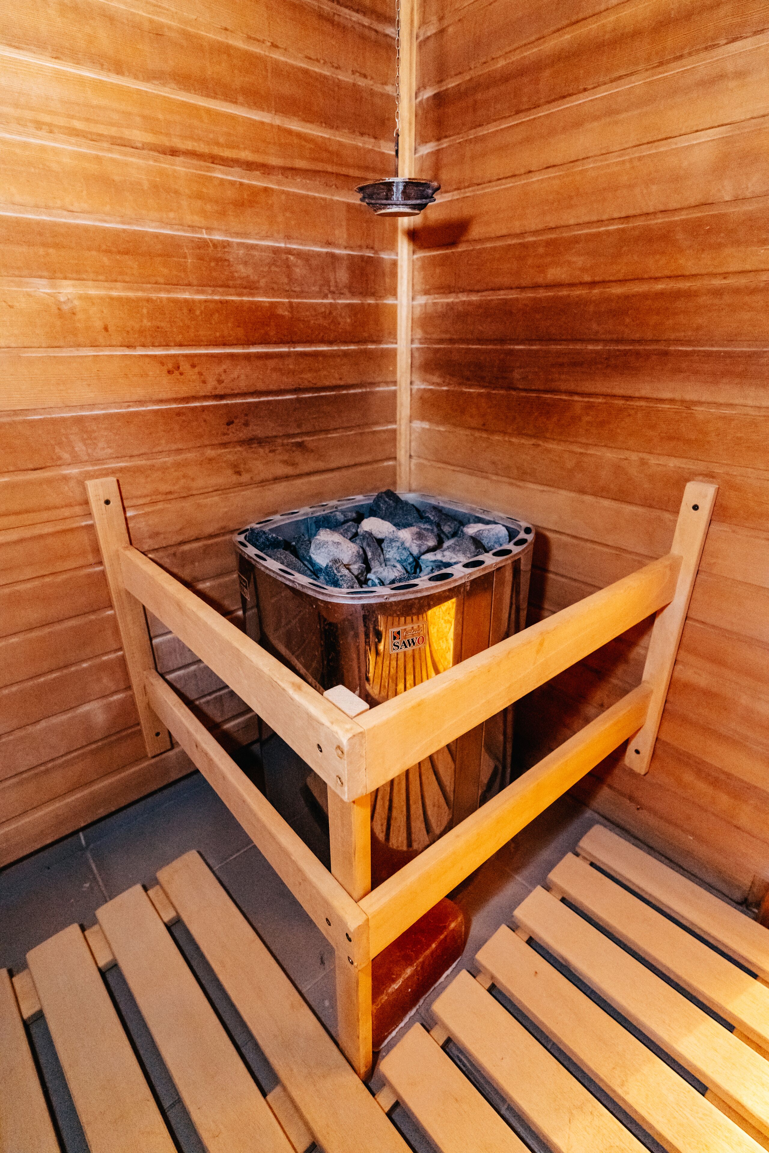 A sauna with a wooden bench and a metal container filled with hot stones.