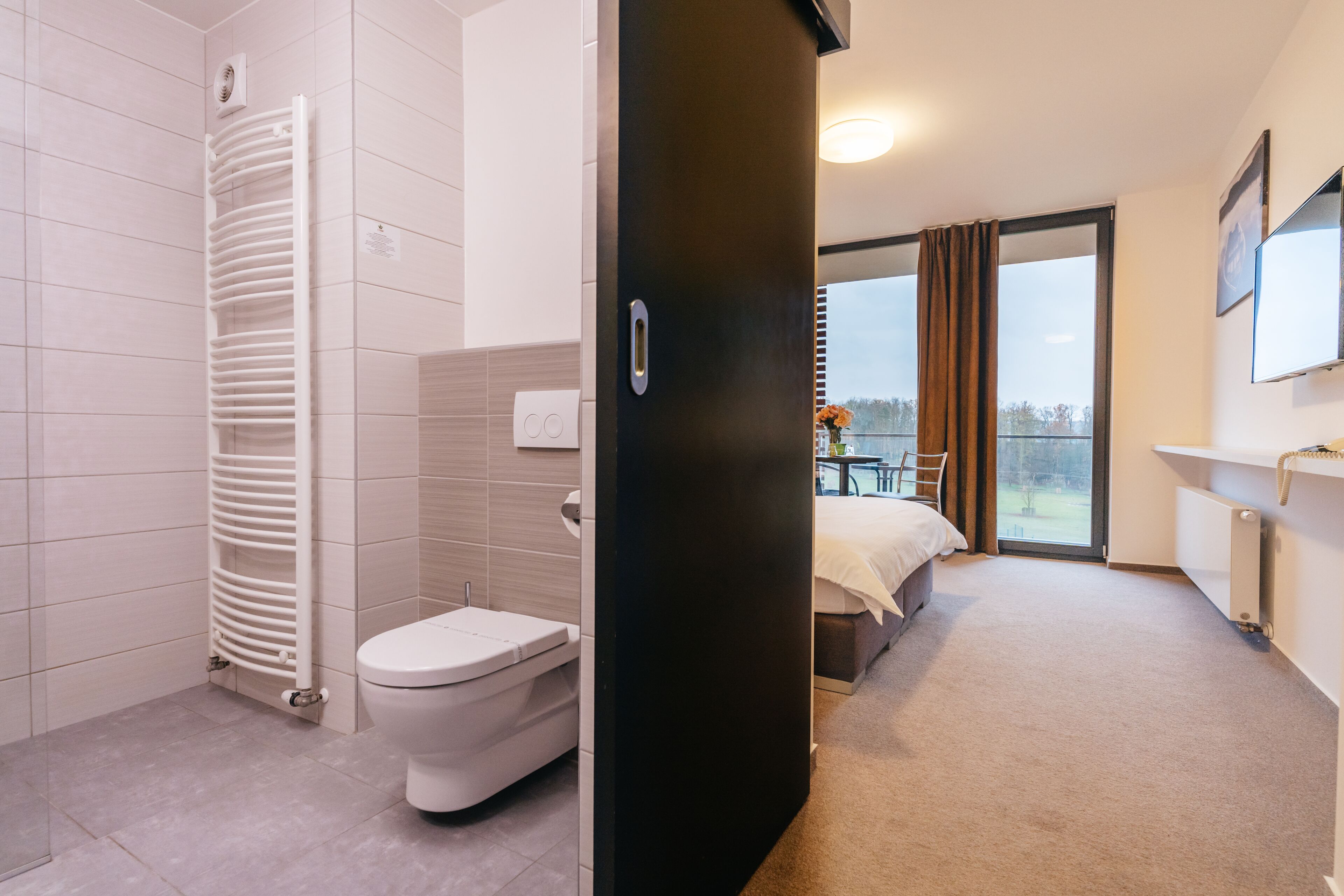 Une salle de bain d’hôtel moderne, équipée de toilettes, d’un radiateur blanc et d’un espace douche.