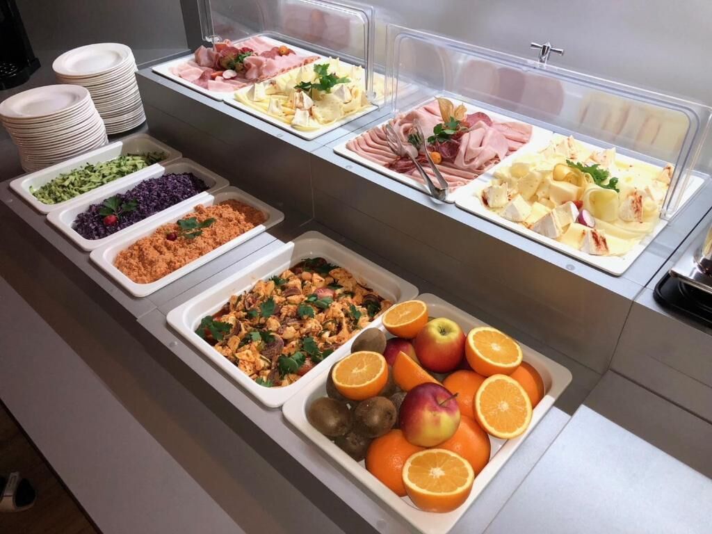 Un bufé con diversas opciones de comida, incluyendo carnes, quesos, frutas y ensaladas.
