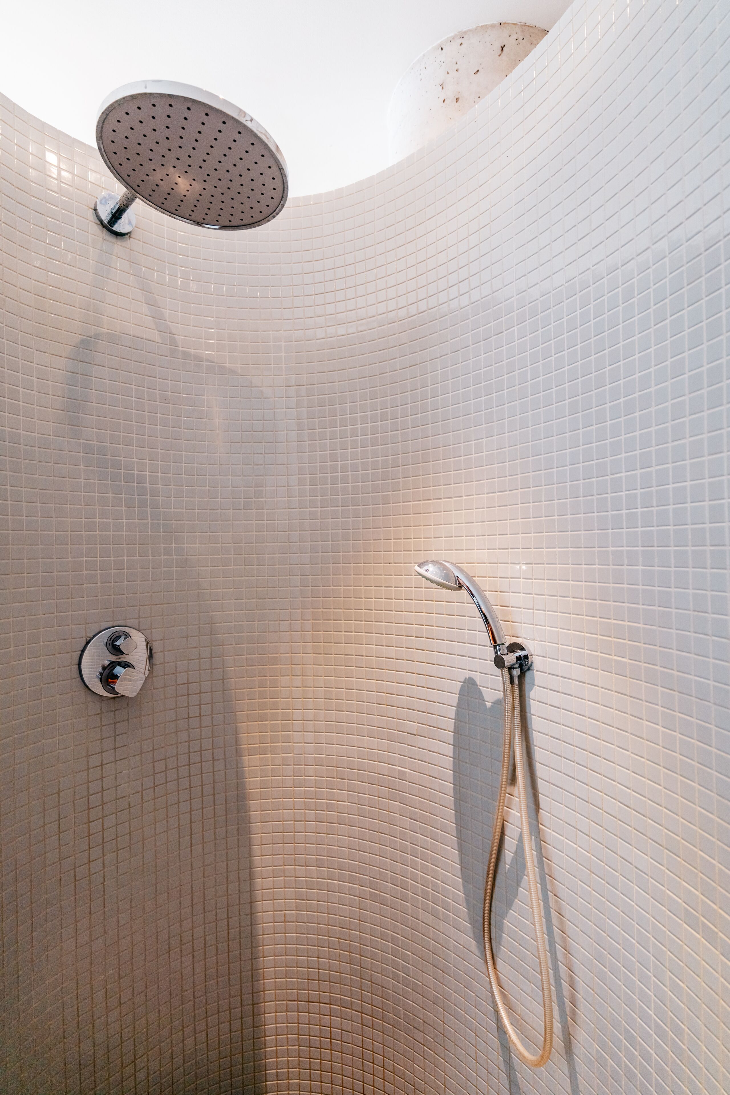 A shower area with a handheld showerhead and a wall-mounted control panel.