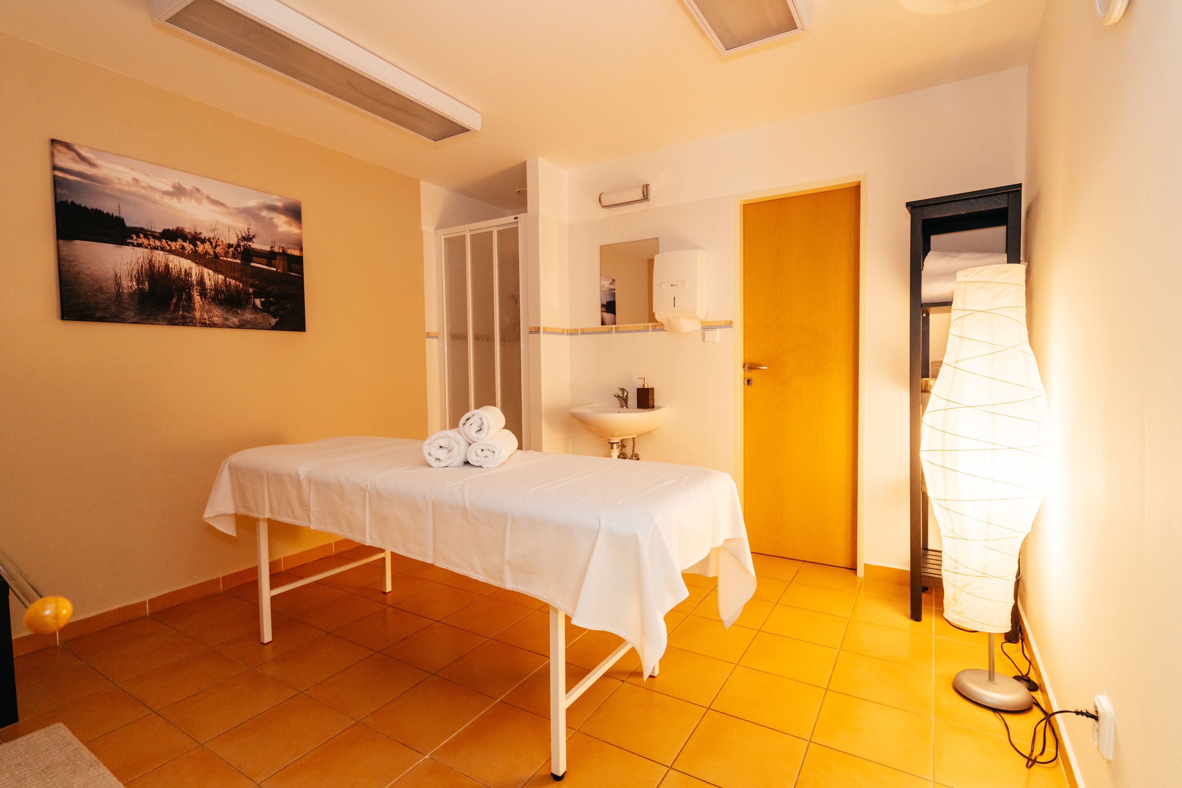 A room with a bed, a sink, a towel rack, and a wall-mounted lamp.