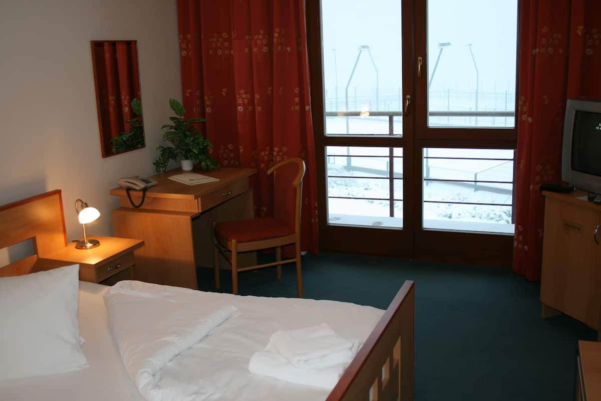 A hotel room with a bed, desk, chair, television, and a window with a view of a snowy landscape.