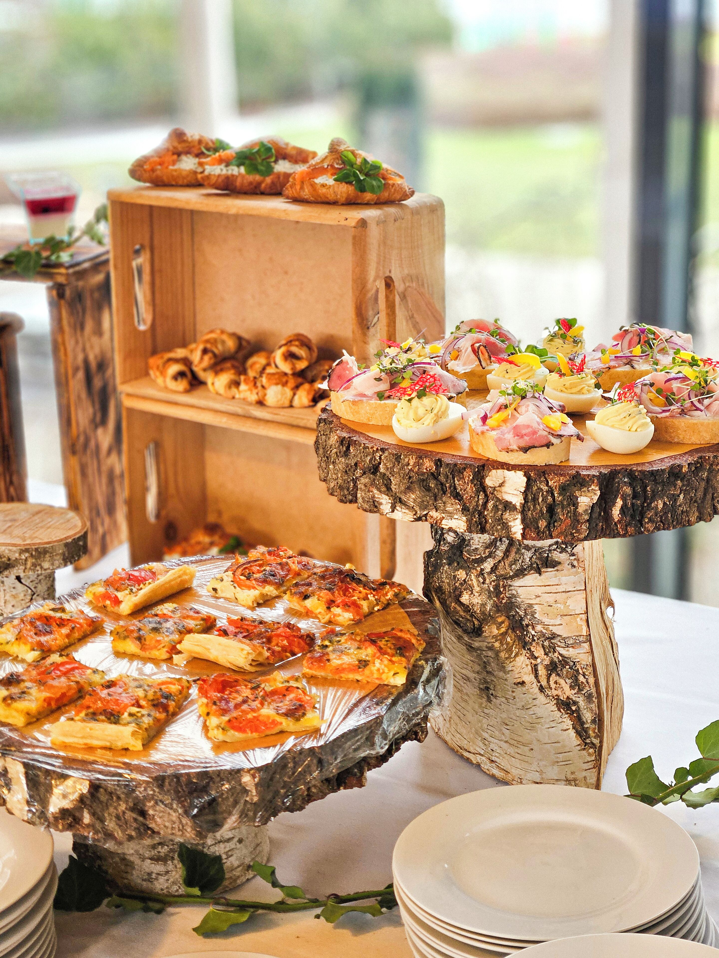 Un buffet proposant une variété de plats, notamment des pizzas et des amuse-gueules, présentés sur des présentoirs en bois et un tronc d’arbre.