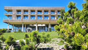 A modern multi-story building with balconies and large windows, surrounded by landscaped gardens and pine trees. - K-Triumf resort (Velichovky)