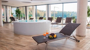 A modern indoor pool area with a hot tub, lounge chairs, and a table with fruit and drinks. - K-Triumf resort (Velichovky)
