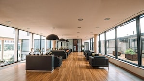 A spacious lobby with a wooden floor, modern seating, and large windows offering views of the outdoors. - K-Triumf resort (Velichovky)