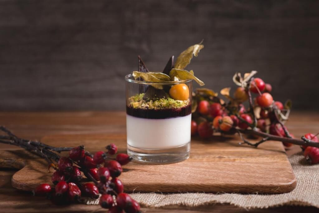 A dessert in a glass on a wooden board, surrounded by branches with berries.