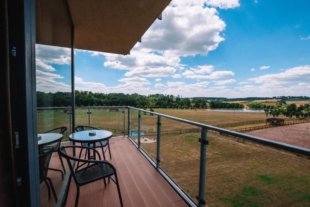 A balcony with a table and chairs, overlooking a grassy field and a body of water.
