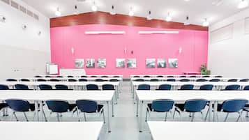 Sala de conferência com mesas brancas e cadeiras azuis, parede rosa com fotografias a preto e branco e luminárias no teto.