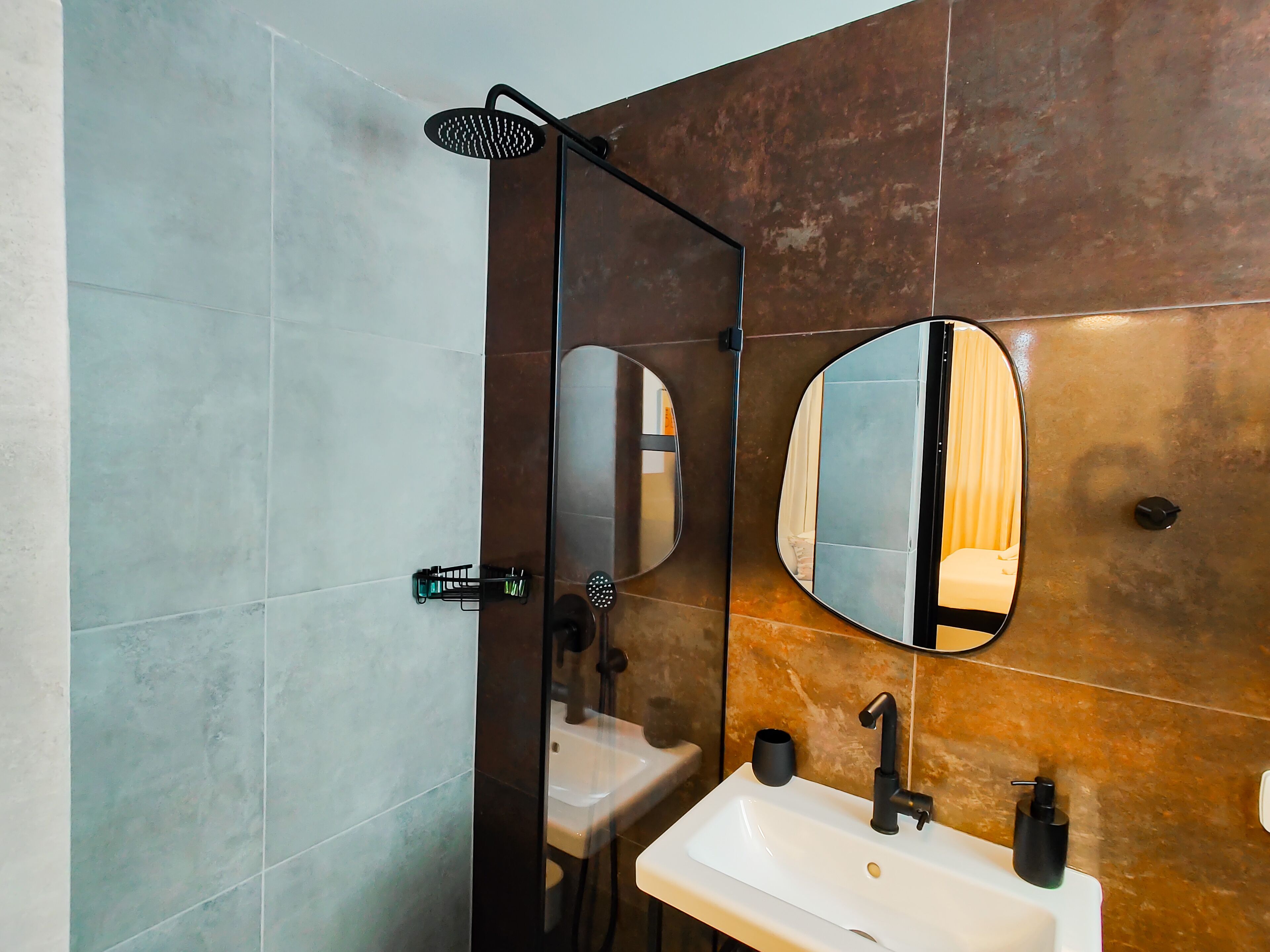 Een moderne badkamer met een douche met glazen wanden, een grote spiegel en een wastafel met een zwarte kraan.