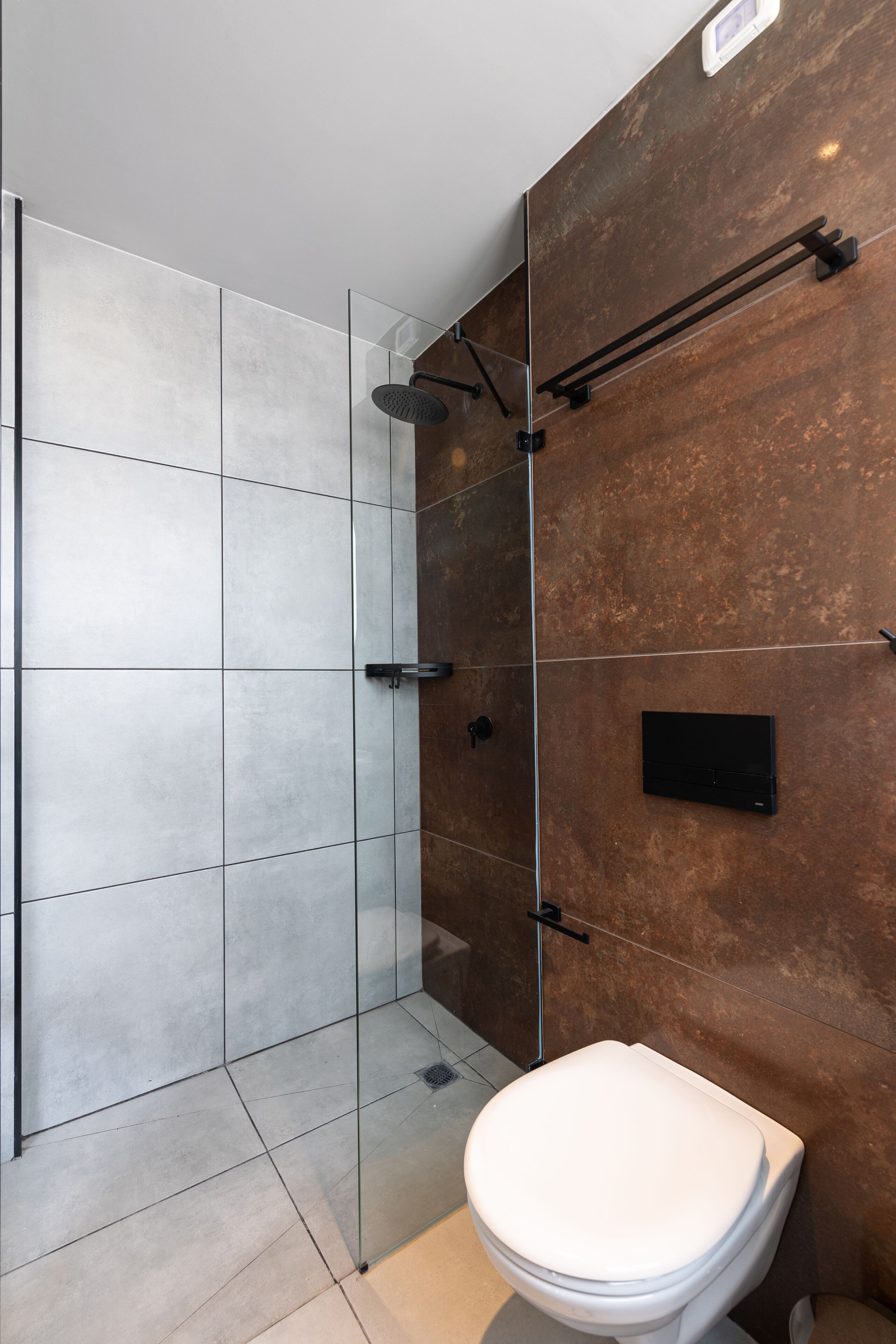Un baño moderno con cabina de ducha de vidrio, inodoro blanco y toallero adherido a la pared.