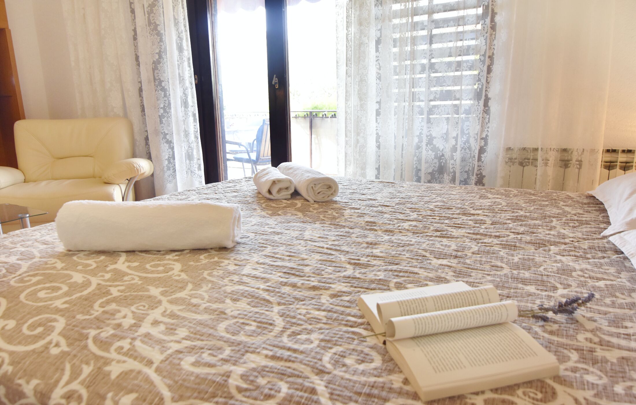 Une chambre d’hôtel avec un grand lit, deux serviettes enroulées et un livre ouvert posé sur le lit.