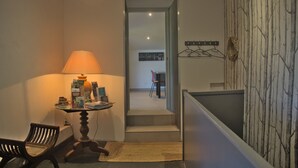 Ein Flur mit einer Lampe, einem Tisch mit Büchern, einem Stuhl und einer Treppe, die in ein weiteres Zimmer führt.