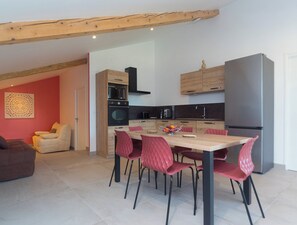 A modern kitchen with a dining area, featuring a wooden table, red chairs, and a large refrigerator.