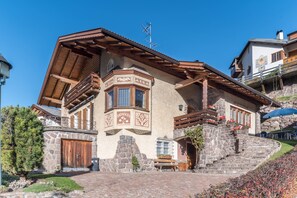 A traditional chalet with a stone facade, wooden balcony, and a stone staircase leading to the entrance.