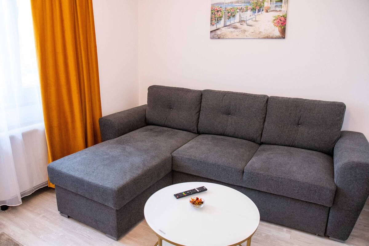 Un sofá seccional gris con una mesa de centro blanca, un control remoto y un cuadro en la pared.