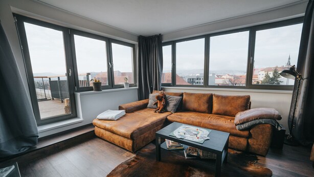 A modern living room with a leather sofa, a coffee table, and large windows offering a city view. - Enjoy panoramic view of The Little Carpathian (Pezinok)