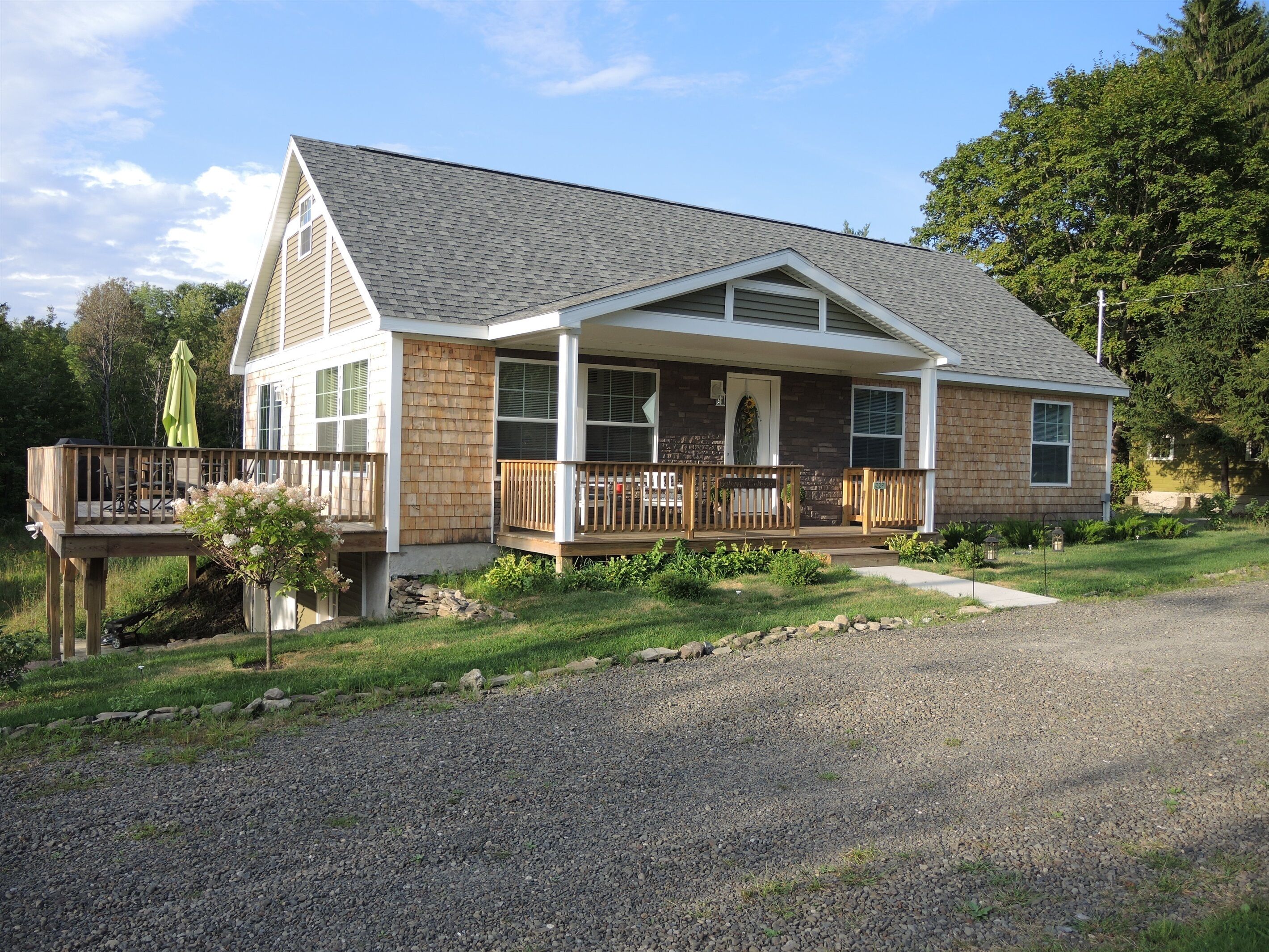 A two-story house with a porch, a deck, and a gravel driveway.