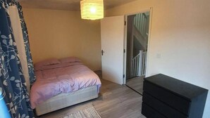 A bedroom with a bed, a bedside table, a door, and a staircase. - 4 Bed House Sleeps 12 - Private Garden - Parking (London)