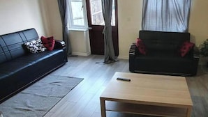 A living room with a black sofa, a wooden coffee table, and a grey rug. - 4 Bed House Sleeps 12 - Private Garden - Parking (London)