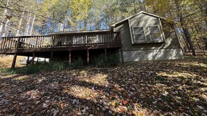 Une cabane dotée d’une terrasse en bois et d’un petit abri attenant, entourée d’une forêt aux feuilles d’automne.