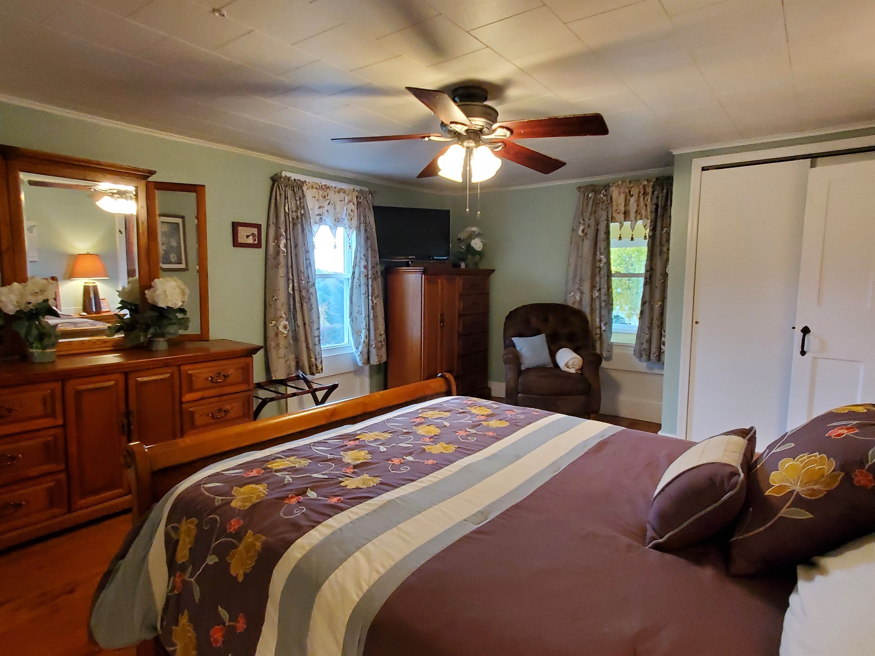 A bedroom with a bed, dresser, chair, and a ceiling fan.