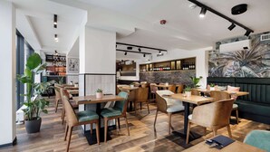 A modern restaurant with wooden flooring, green upholstered chairs, and a bar area with a brick wall. - Kyriad Stargard (Stargard Szczecinski)