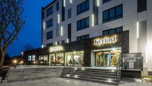 A modern hotel with multiple floors, a visible staircase leading to the entrance, and illuminated signage for 'Céline' and 'Kyrjad' brands. - Kyriad Stargard (Stargard Szczecinski)