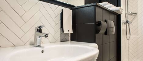 Un baño moderno con un lavamanos blanco, un espejo encima y una zona de ducha.
