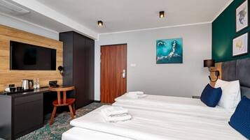 A hotel room with a bed, a desk, a chair, a television, and artwork on the walls.