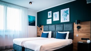 A double bed with a grey headboard, two wall-mounted lamps, and a world map artwork on the wall. - Kyriad Stargard (Stargard Szczecinski)