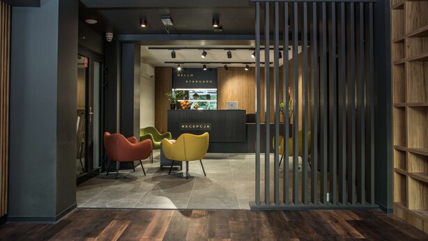 A reception area with a modern design, featuring a reception desk, a counter with a sign, and several colorful chairs. - Kyriad Stargard (Stargard Szczecinski)