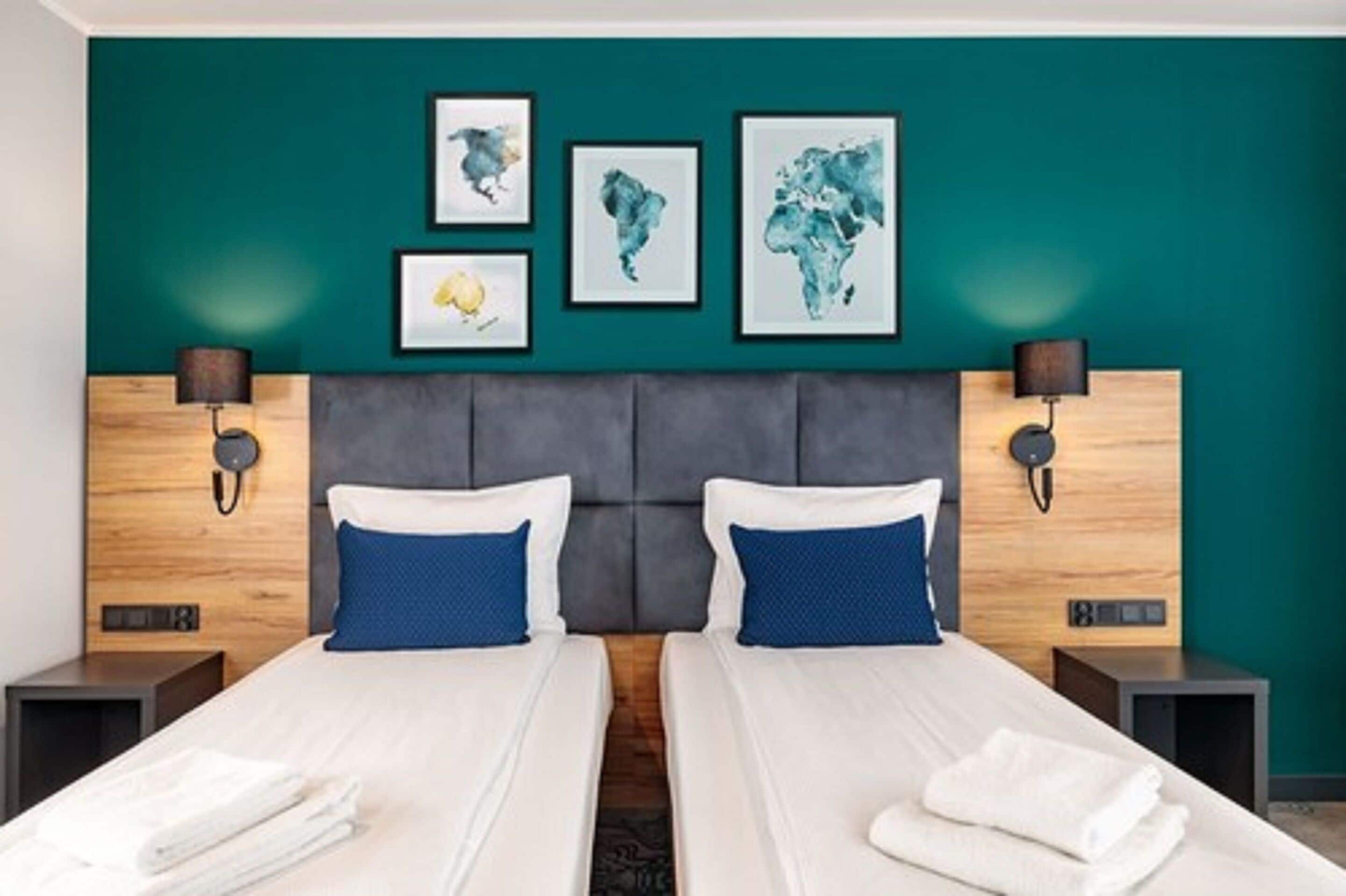 A hotel room with two beds, teal walls, and artwork on the wall.