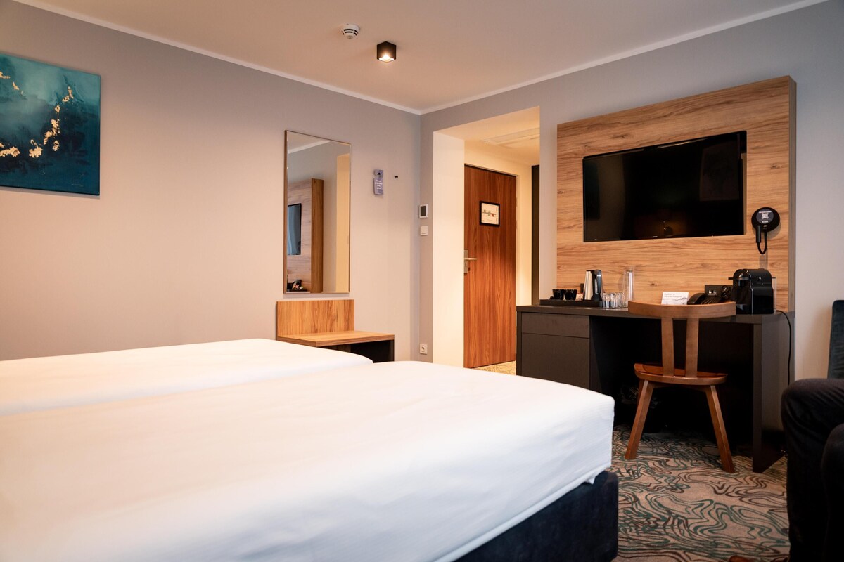 Habitación de hotel con una cama grande, un escritorio con televisor, un espejo y un panel de pared de madera.
