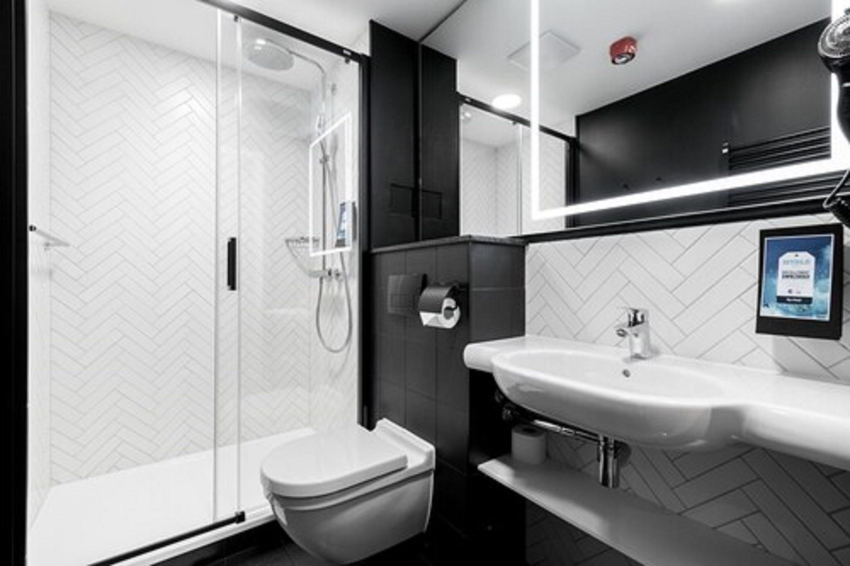 Un baño moderno con ducha envuelta en vidrio, un lavamanos blanco y un mueble negro.