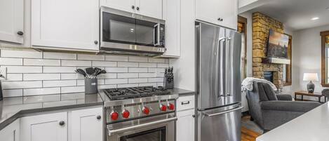 Una cocina moderna con gabinetes blancos, electrodomésticos de acero inoxidable y una chimenea de piedra.