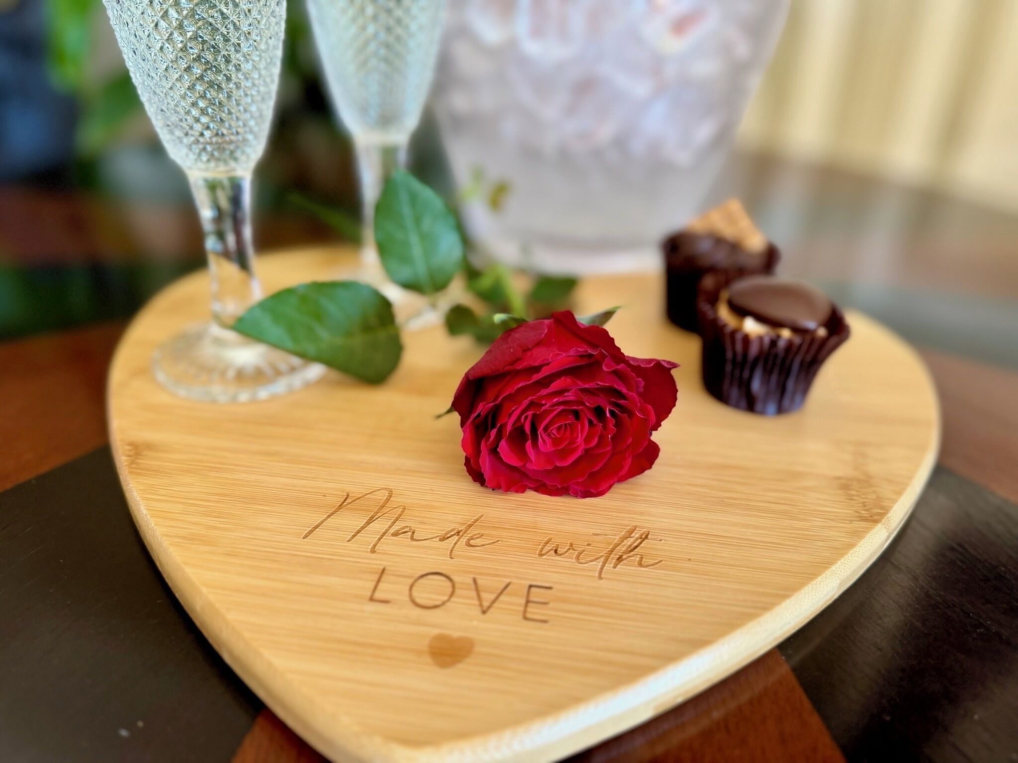 A wooden heart-shaped serving board with the inscription "Made with LOVE" and a red rose.