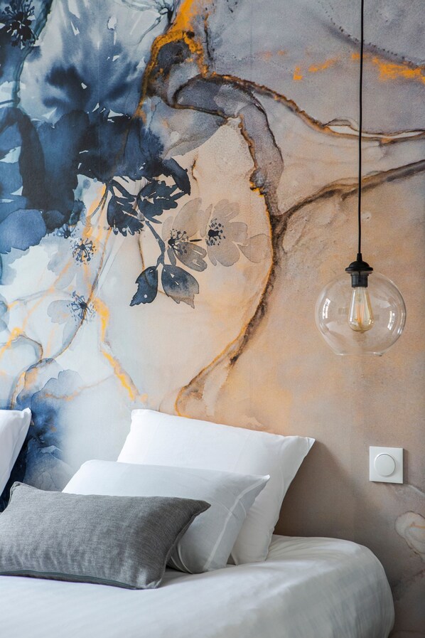 A bedroom with a bed, pillows, a wall mural, and a hanging light fixture.