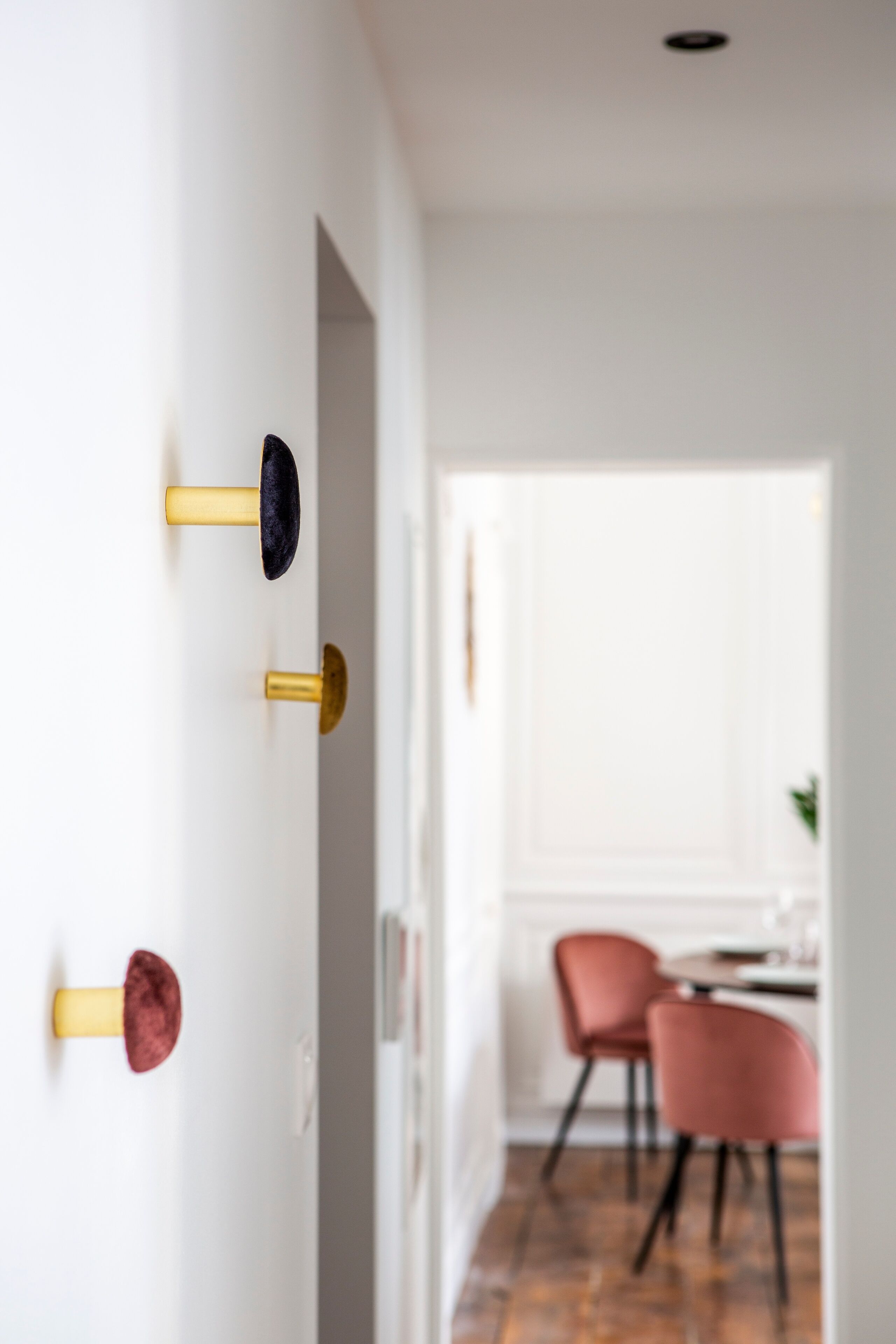 Un couloir avec un mur blanc, une porte dotée d’une poignée dorée et un coin repas avec des chaises rouges et une table.