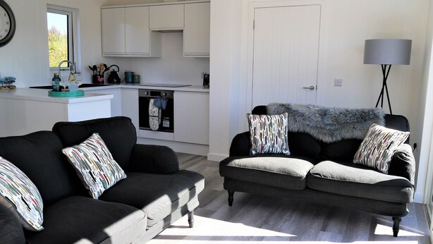 A modern living room with a sofa set and a kitchen in the background. - Sea Glass -  a lodge that sleeps 4 guests  in 2 bedrooms (Gatehouse of Fleet)