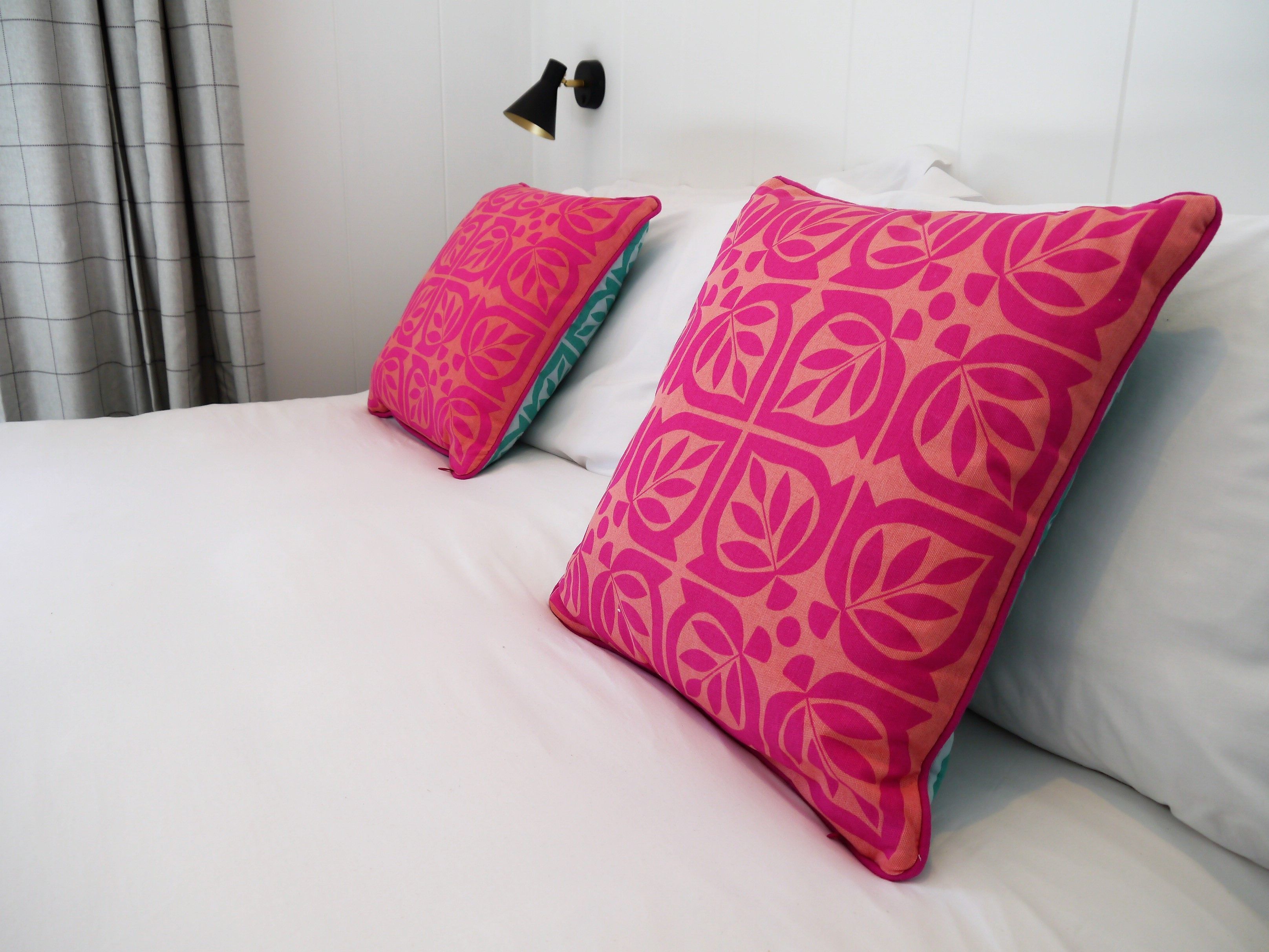 A bed with white bedding and two large pillows with a pink and orange leaf pattern.