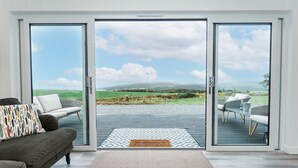 Un intérieur moderne avec un canapé, un tapis à motifs et une vue sur une terrasse extérieure, accessible par des portes vitrées.
