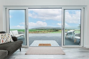 Een modern interieur met een bank, een vloerkleed met patroon en uitzicht door glazen deuren op een terras.
